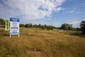 Affordable brick home development site near Joseph's Creek, open land with trees and blue sky.