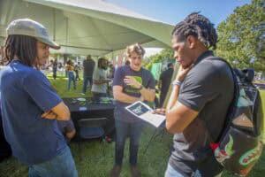 Outdoor community event with young people engaging in conversation and activities at a sunny park.