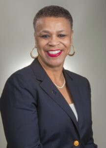 Empowered professional woman smiling in formal navy blazer and jewelry for business or news profile.