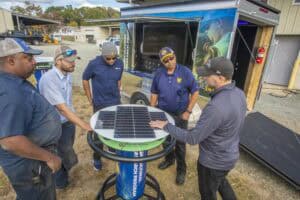 Solar energy demonstration with a group of professionals around a portable solar panel station.