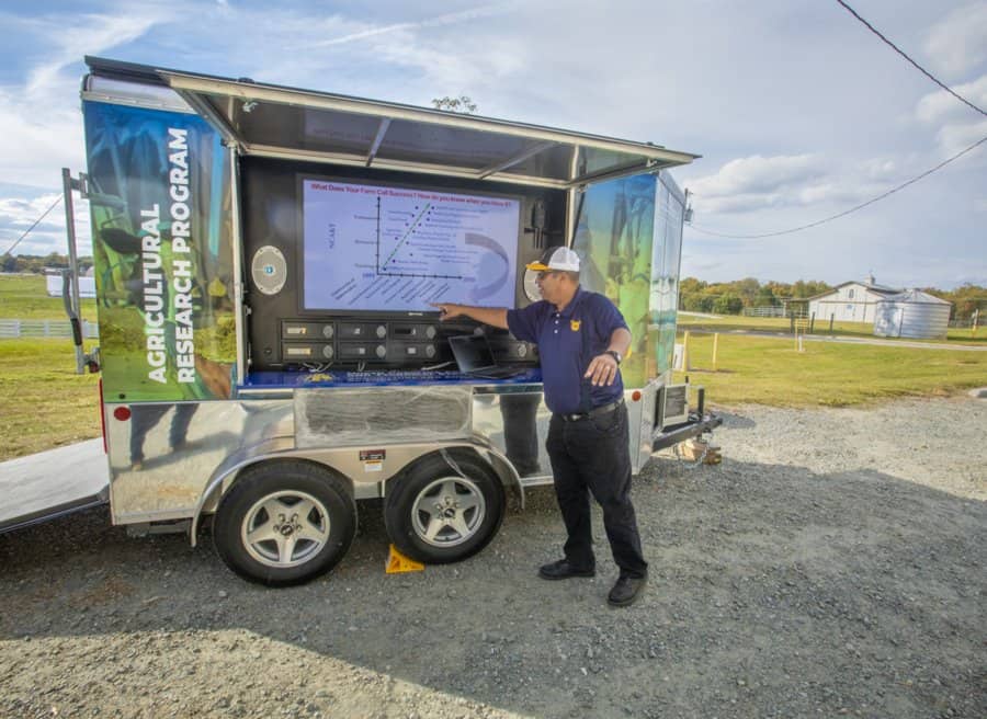 Soil scientist presenting agricultural research data on a mobile trailer at an outdoor research site.