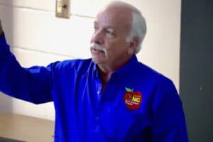 Voter giving a speech at a political event wearing a blue shirt with NC logo.