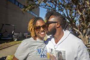A woman and man smiling outdoors on a sunny day, engaging in a friendly conversation.