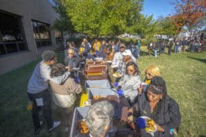 Community outdoor food event with diverse people serving and enjoying meals on a sunny day.