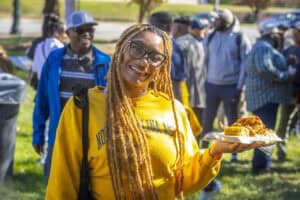 A woman with dreadlocks and glasses holding a plate of food at an outdoor event.