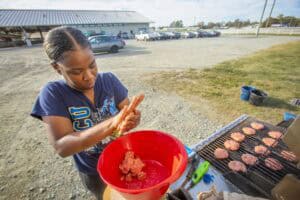Grilling hamburgers outdoors with a young girl preparing meat for the barbecue.