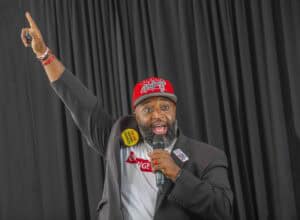Empowered speaker at rally with microphone, raising hand, inspiring audience, black curtain backgrou.