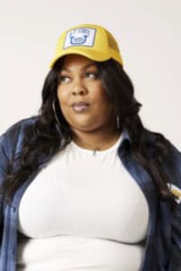 "Woman wearing yellow CAES News cap and denim jacket, looking to the side, promoting news and update.