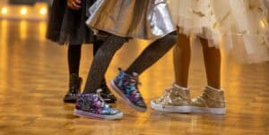Colorful sneakers and sparkly shoes worn by children, dancing on a polished wooden floor.