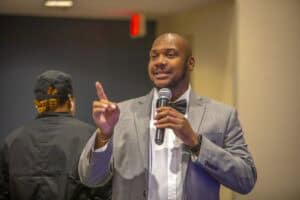 Engaged male speaker at conference delivering presentation with microphone and confident gesture.