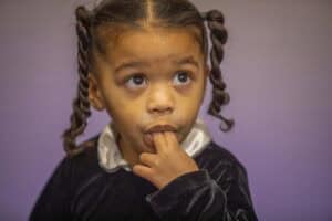 A child with braided hair looking up thoughtfully against a purple background.