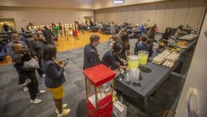 Attendees enjoying food and drinks at a conference buffet in a large event hall.