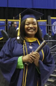Graduation student in cap and gown holding diploma at ceremony.