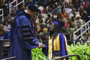 Graduation ceremony with graduate receiving diploma from university official.