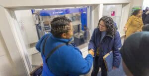 Two women shake hands in a professional setting, with one wearing glasses and a blue jacket, and the other smiling.