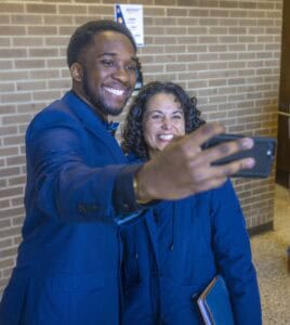 Two smiling individuals take a selfie together in a well-lit indoor space.