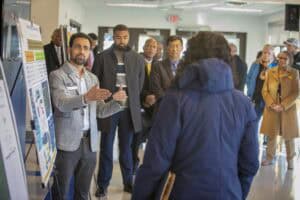 A presenter engages with an audience in a discussion, while several people listen attentively in the background.