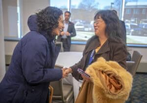 Engaged women shaking hands at a professional event in a conference room.
