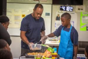 Man and boy cooking together in a community kitchen or cooking class setting.