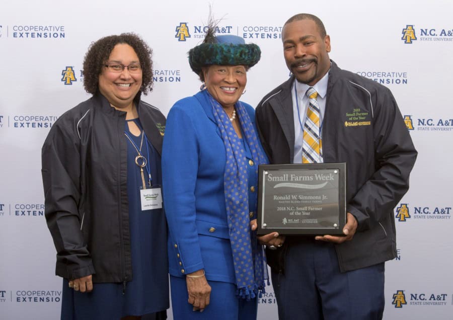 Group of three people at an award ceremony, smiling and holding a plaque.