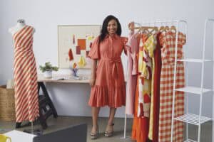 A woman standing next to a clothing rack with colorful dresses and a mannequin displaying a striped.