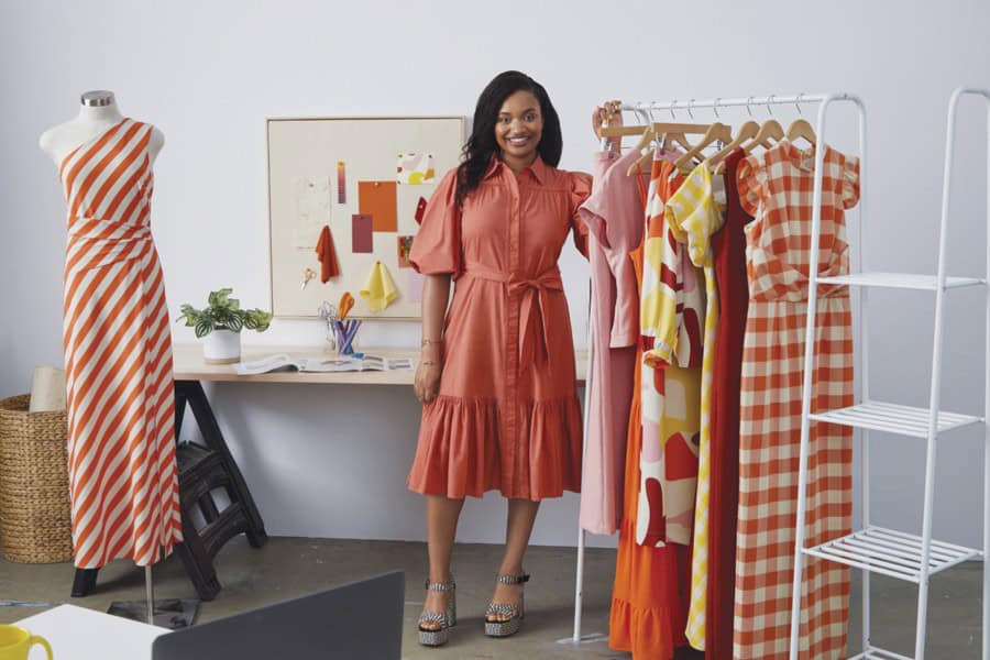 A woman standing next to a clothing rack with colorful dresses and a mannequin displaying a striped.