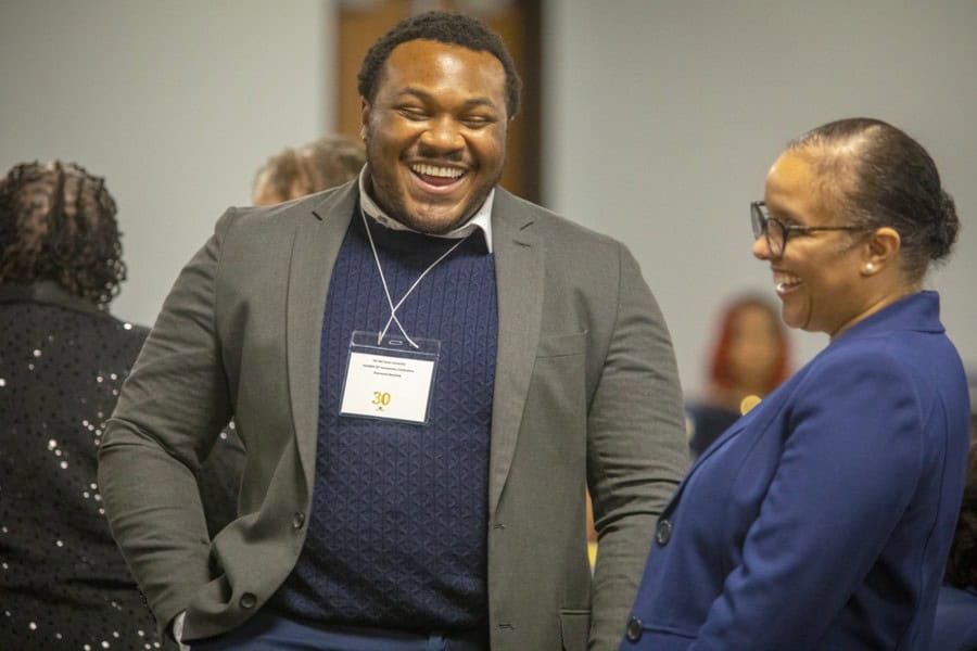 Two smiling people engage in conversation at an event, one wearing a blazer with a name tag.