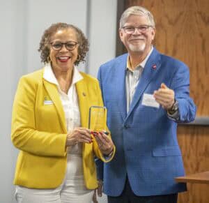 Two people stand together, one holding a clear award, smiling and engaged in conversation.
