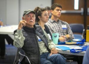 A group of attendees engaged during a meeting, focusing on a speaker or presentation.