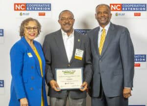 Three people pose together at an event, holding a certificate of appreciation for Small Farms Week.