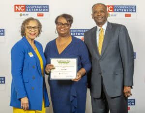 Three people pose together, smiling, with one holding a certificate for Small Farms Week recognition.