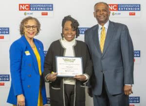 Three individuals pose together, one holding a certificate of appreciation for Small Farms Week.