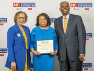 Three people in professional attire celebrate Small Farms Week, holding a certificate of appreciation.
