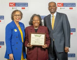Three individuals pose together, smiling and holding a certificate for Small Farms Week recognition.
