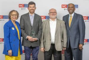 Four professionals pose together, one holding an award, against a backdrop promoting NC Cooperative Extension.
