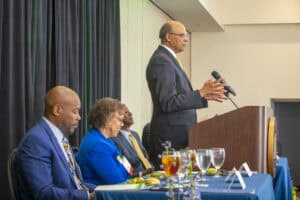 Elevated view of a man speaking at a conference podium with seated panelists listening attentively.