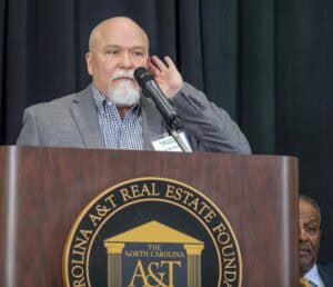Man speaking at a podium with Carolina A&T logo during a conference or event.