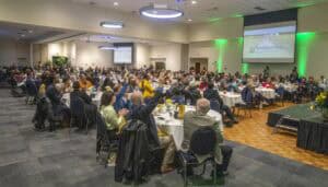 Large conference with diverse attendees at CAES News event in a spacious hall.
