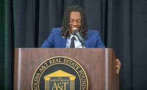 A man speaking at a podium with the A&T North Carolina logo during a formal event.