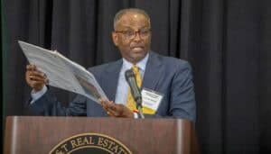 A man in a suit speaking at a conference with a microphone and holding a newspaper.