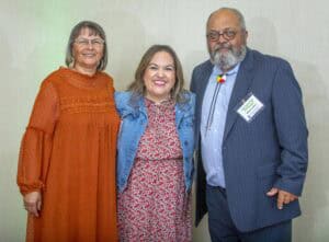 A woman in an orange dress, a woman in a red floral dress with a denim jacket, and a man in a blue s.