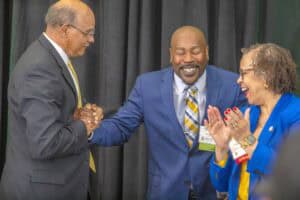 Three professionals smiling and shaking hands at a conference event.