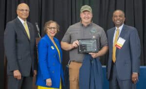 Four individuals celebrate an award presentation for Small Farms Week, with one holding a plaque.