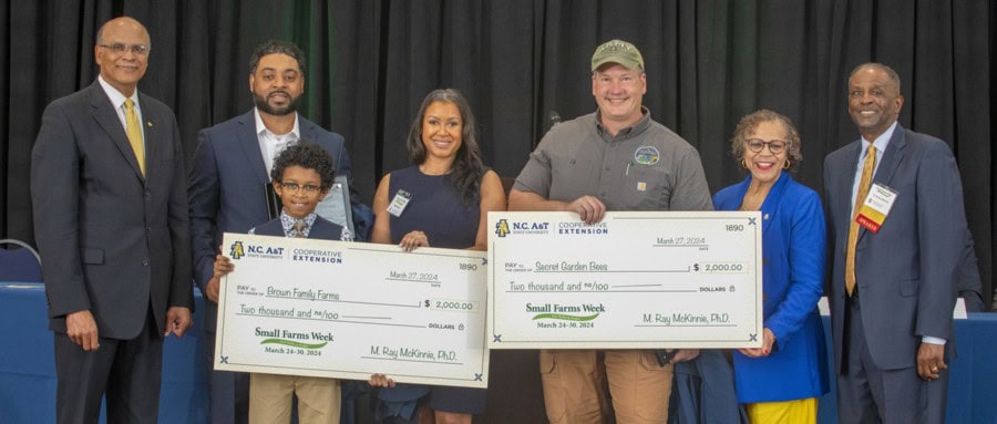 A group of six people holds oversized checks for $2,000 each, celebrating Small Farms Week awards.