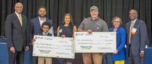 Six people gather with oversized checks for $2,000 each, celebrating Small Farms Week at an event.