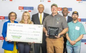 Group photo celebrating Small Farms Week, featuring award recipients with a check and plaque for Secret Garden Bees.
