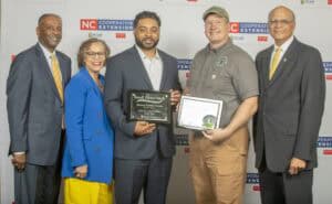 Five people celebrate "Small Farms Week" with awards, smiling and standing in front of a cooperative extension backdrop.
