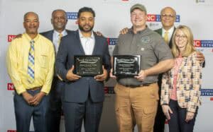 Seven people gather to celebrate Small Farms Week, holding award plaques for achievements in farming.