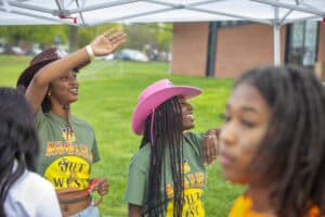 Cheerful young women wearing green shirts and pink hat enjoying outdoor event at CAES News gathering.