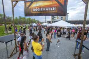 Crowd gathered at Aggie Ranch outdoor event with large sign and tents.